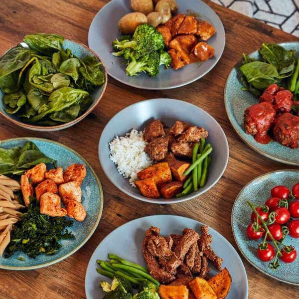Macro Based Diet 2200 Calorie Weekly Meal Prep Plan with balanced portions of grilled chicken, rice, roasted sweet potatoes, leafy spinach, broccoli, cherry tomatoes, and meatballs on a wooden table setting.